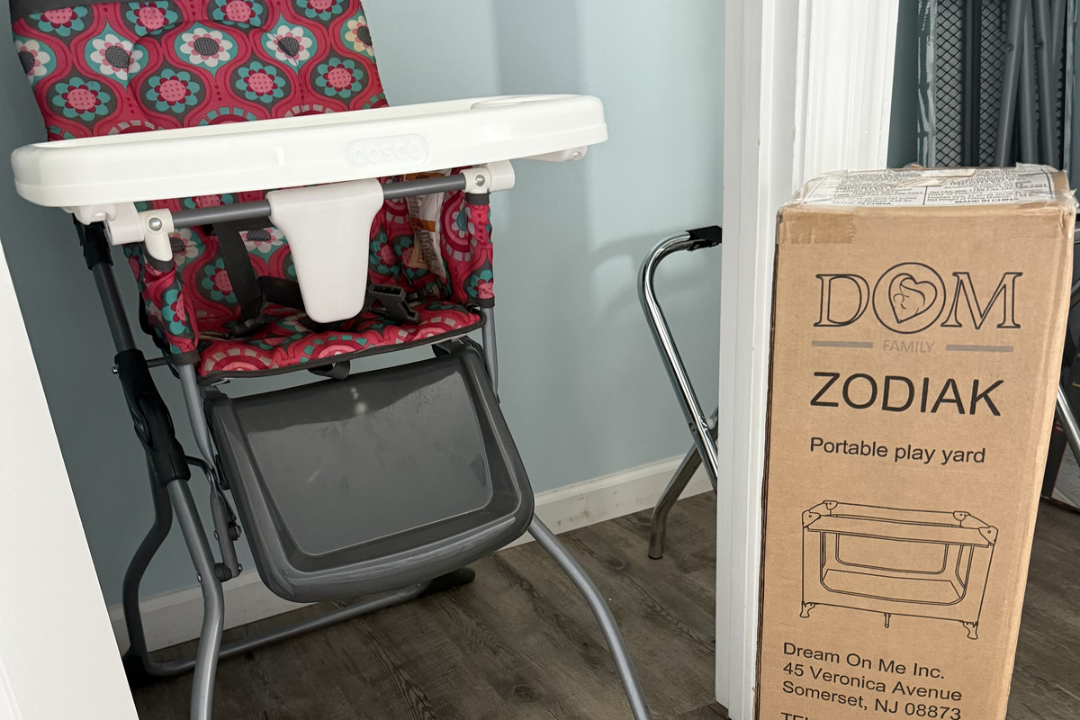 Highchair and Pak N Play in guest closet with an ironing board and box fan. 