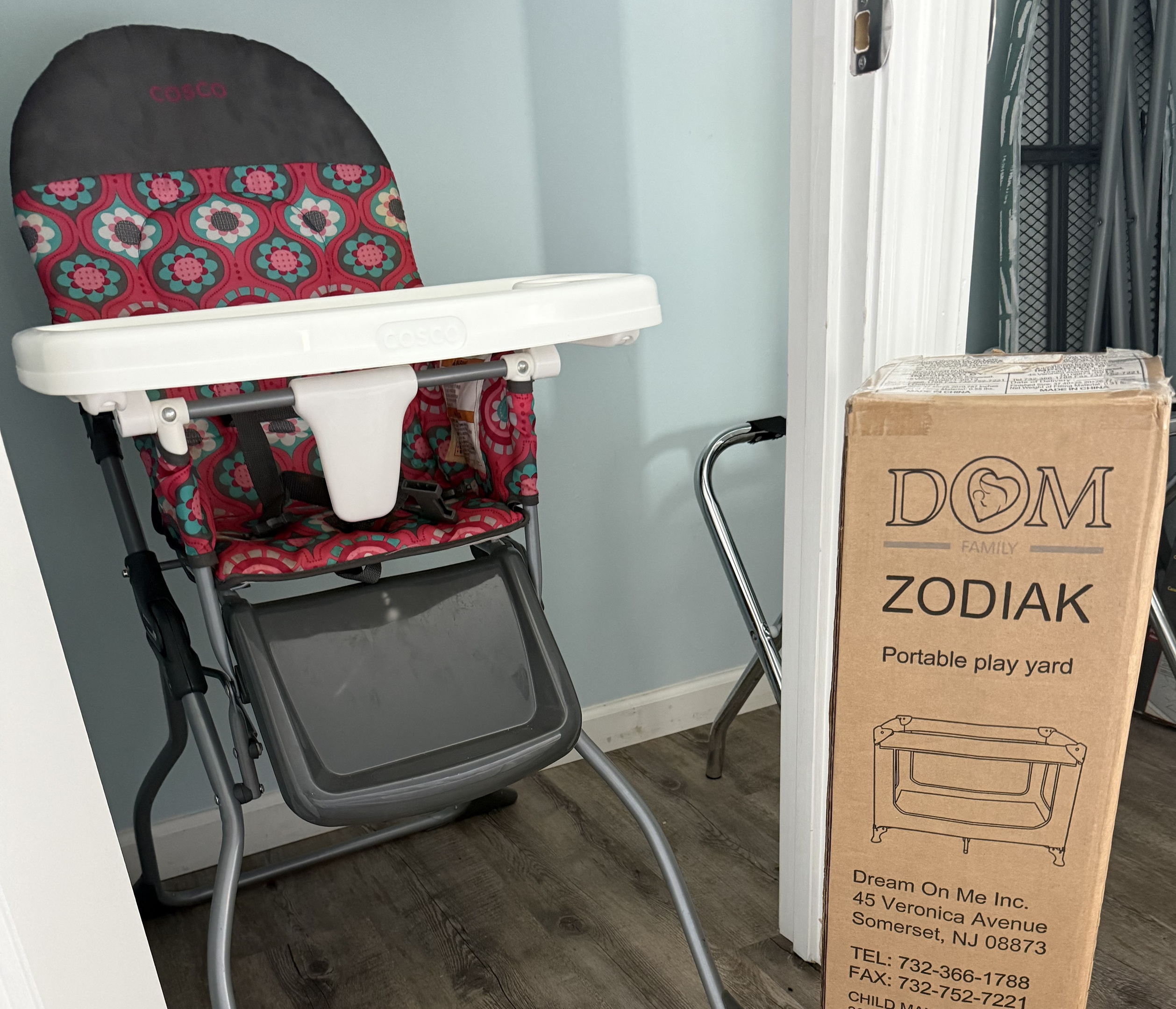 Highchair and Pak N Play in guest closet with an ironing board and box fan. 