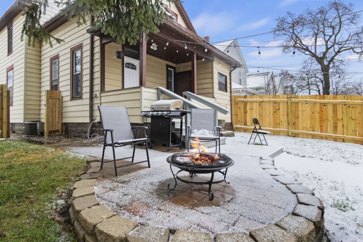 Beautiful patio featuring a central table surrounded by chairs, a cozy seating arrangement, lush trees adding natural charm, and a house backdrop—perfect for outdoor dining and relaxation in a serene setting