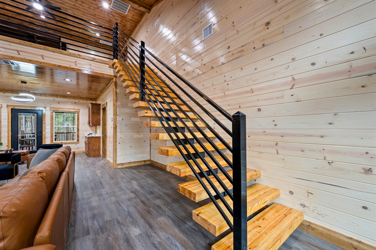A staircase with sleek railing leads up to the loft and additional sleeping spaces, adding to the cabin’s open feel.