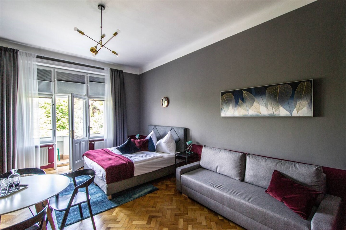 Apartment bedroom with big comfy bed , balcony, dining table and large sofa.