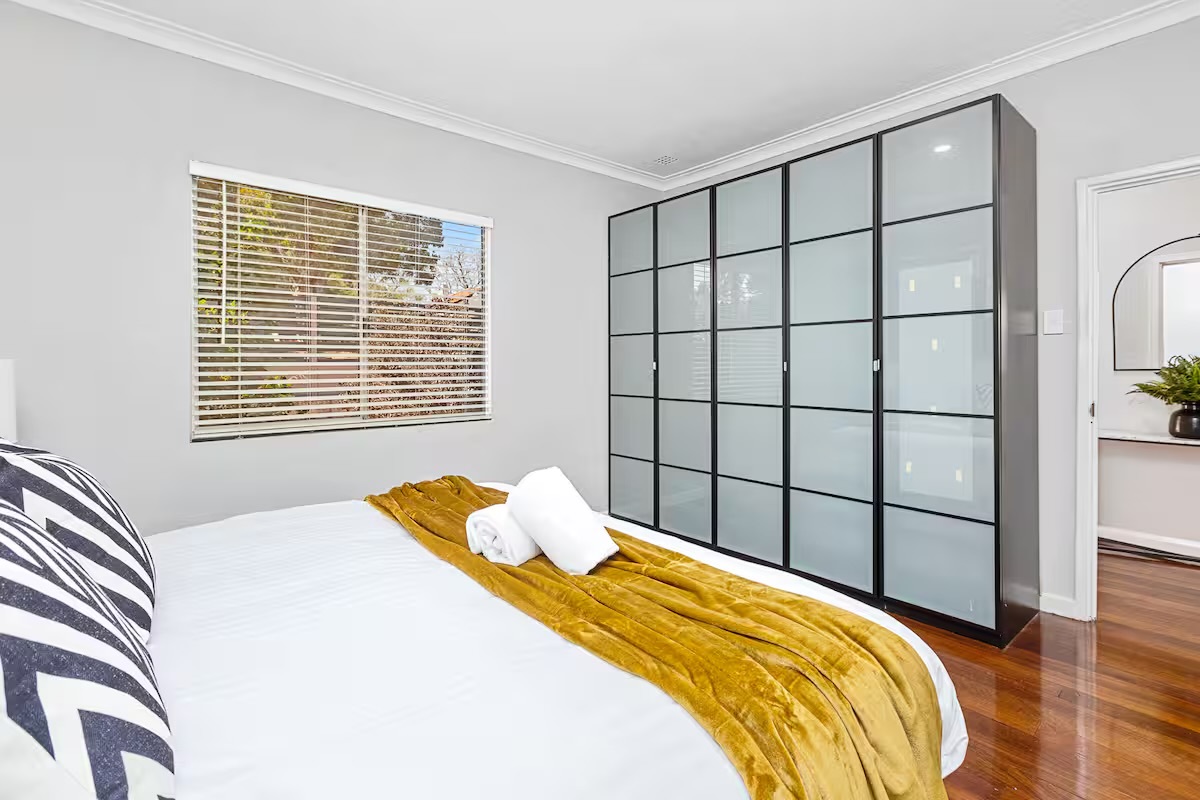 This bedroom at Sasha’s Cottage on the Hill includes wall-length wardrobe storage, a bright window and polished timber floors for a practical stay.