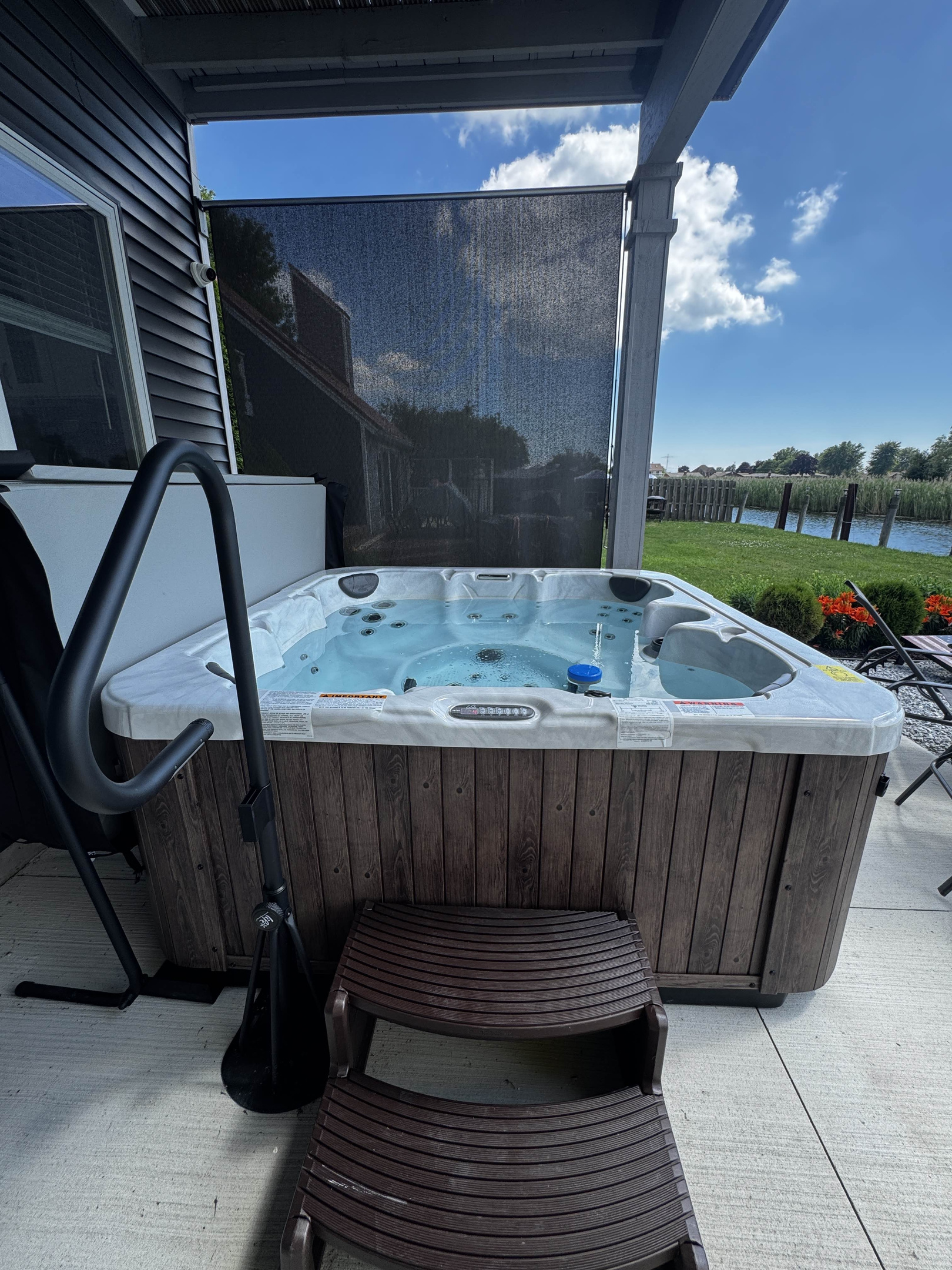 Enjoy easy access to this private outdoor hot tub, featuring built-in steps and a sturdy handrail for comfort and convenience. Perfectly set on a waterfront patio, it offers a relaxing spa experience surrounded by fresh air and peaceful canal-side views.