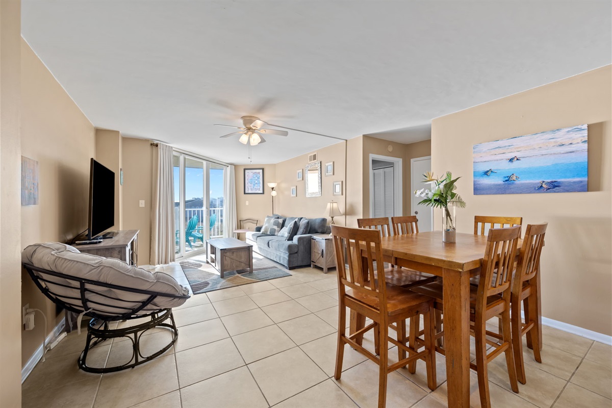 Open living and dining area with seating for meals, comfortable lounge space, and sliding doors leading to the oceanfront balcony