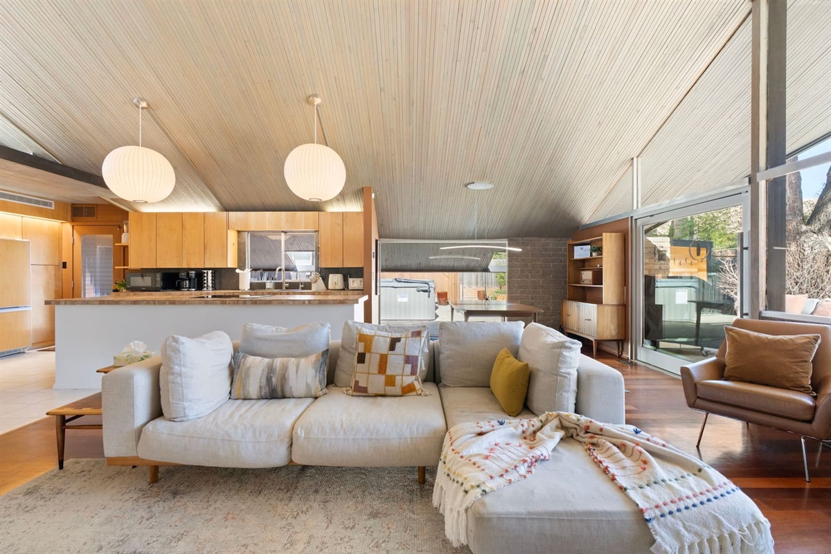 Bright open-concept living space with vaulted wood ceilings, cozy modern seating, and seamless indoor-outdoor flow.