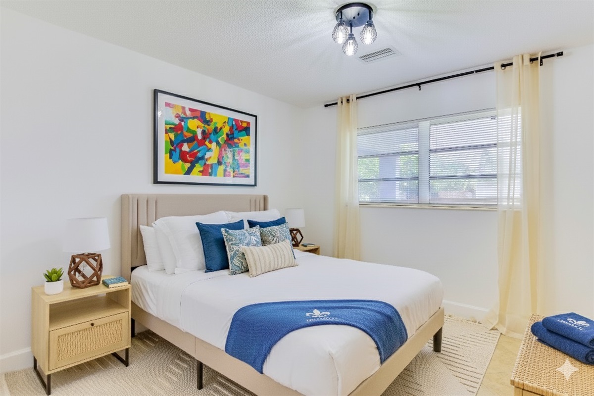 This serene guest bedroom features a plush queen bed with hotel-quality linens, soothing coastal accents, and soft natural light filtering through sheer curtains—perfect for a restful night’s sleep.