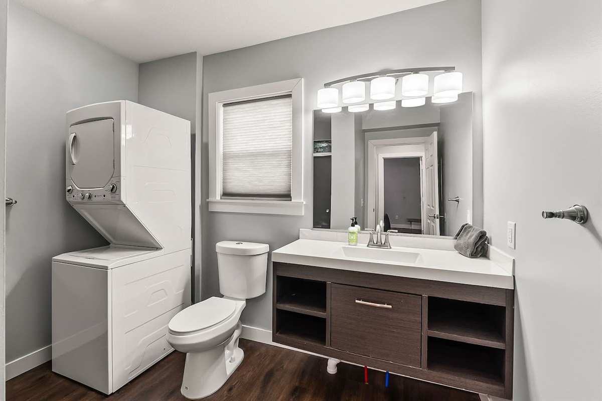 Modern full bathroom featuring a sleek vanity, bright lighting, toilet, and in-unit washer and dryer for added convenience.