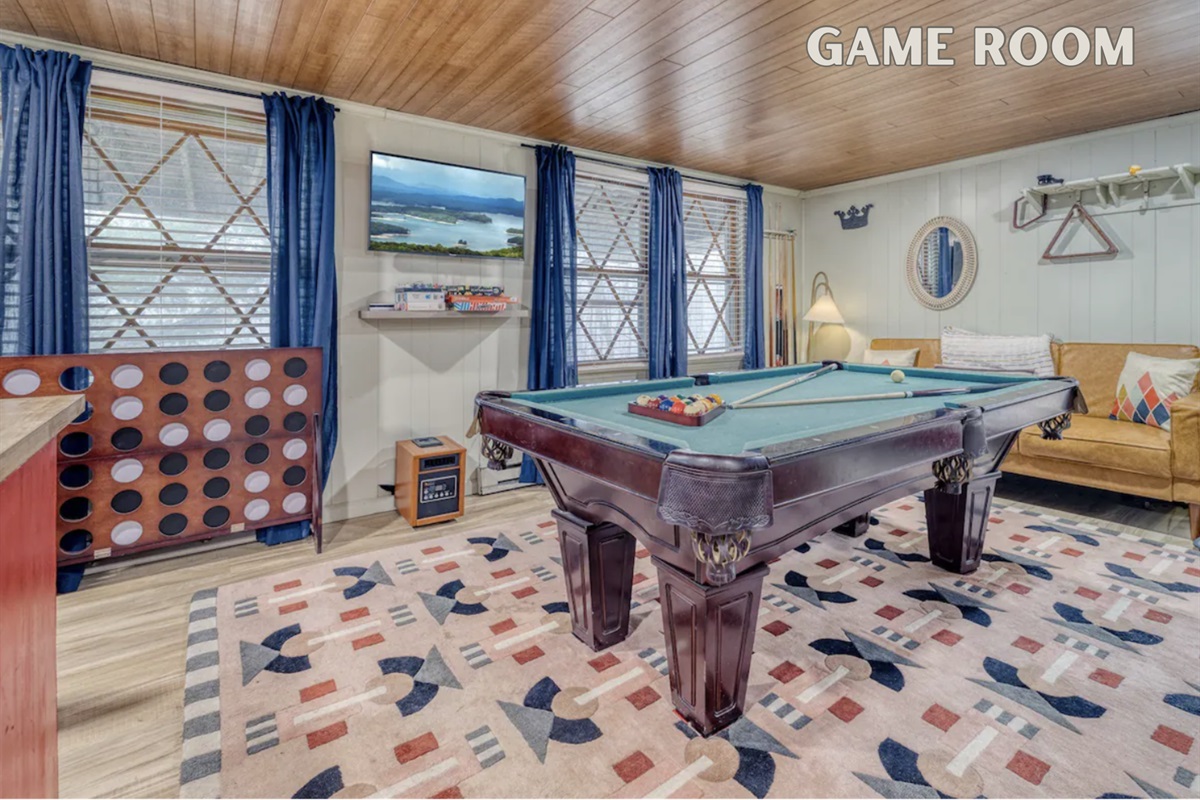 The game room at 'A-Frame of Mind' features a pool table, TV, oversized Connect Four, cozy seating, and board games. Perfect for unforgettable family moments and friendly competition.