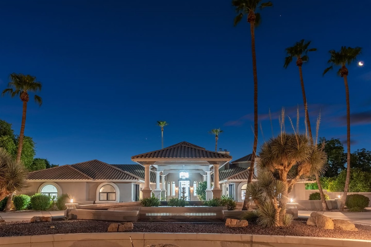 A breathtaking view of the estate illuminated under a desert night sky—complete with palm trees and elegant architectural symmetry.

