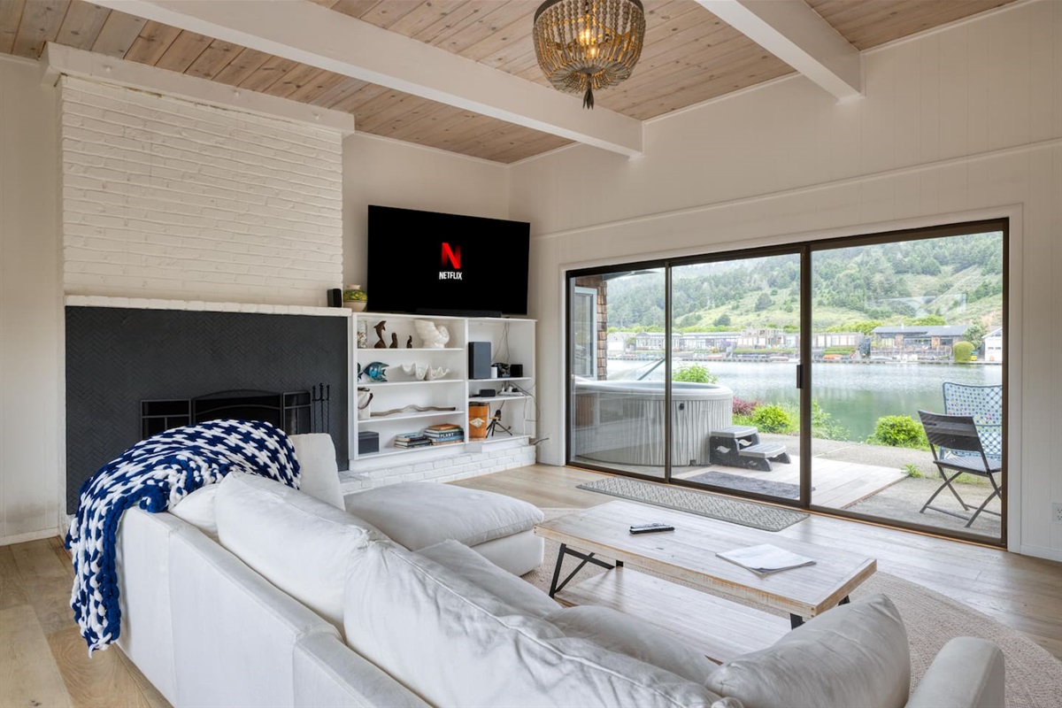 - Cozy living room with white sectional and sliding doors to the waterfront  
- Wall mounted TV with streaming access for entertainment anytime  
- Large windows flood the space with natural light and scenic views  
