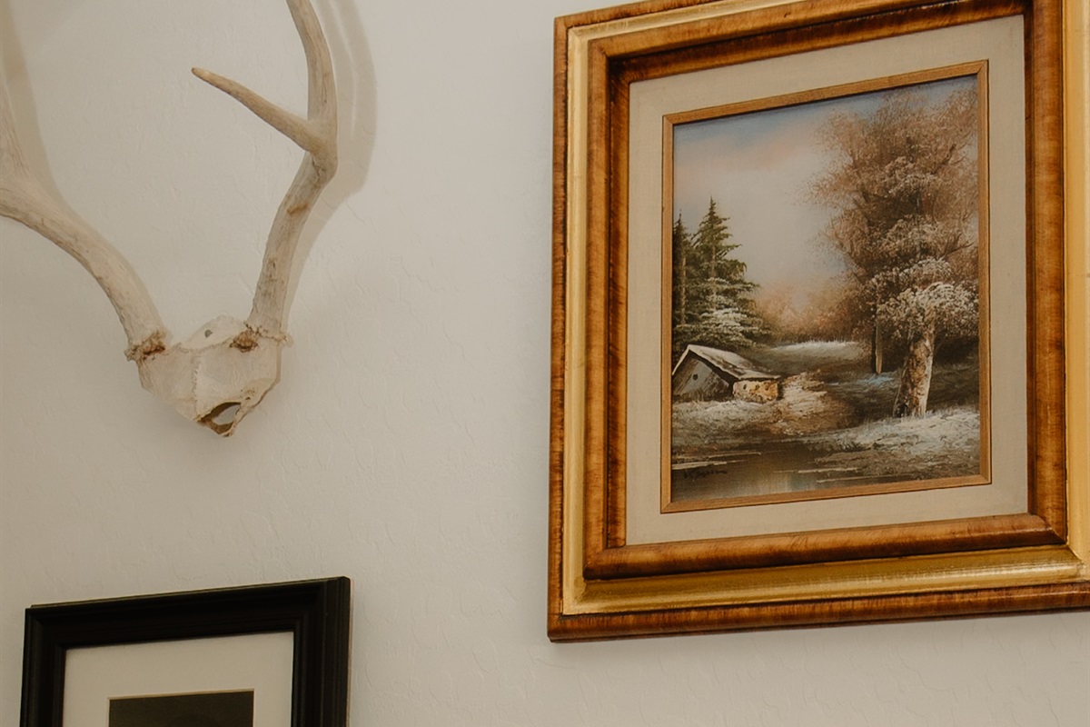 Curated gallery wall with vintage landscape art and shed antlers in this Pinetop-Lakeside luxury townhome. Authentic Arizona hunting lodge character throughout this White Mountains vacation rental with thoughtful design details.