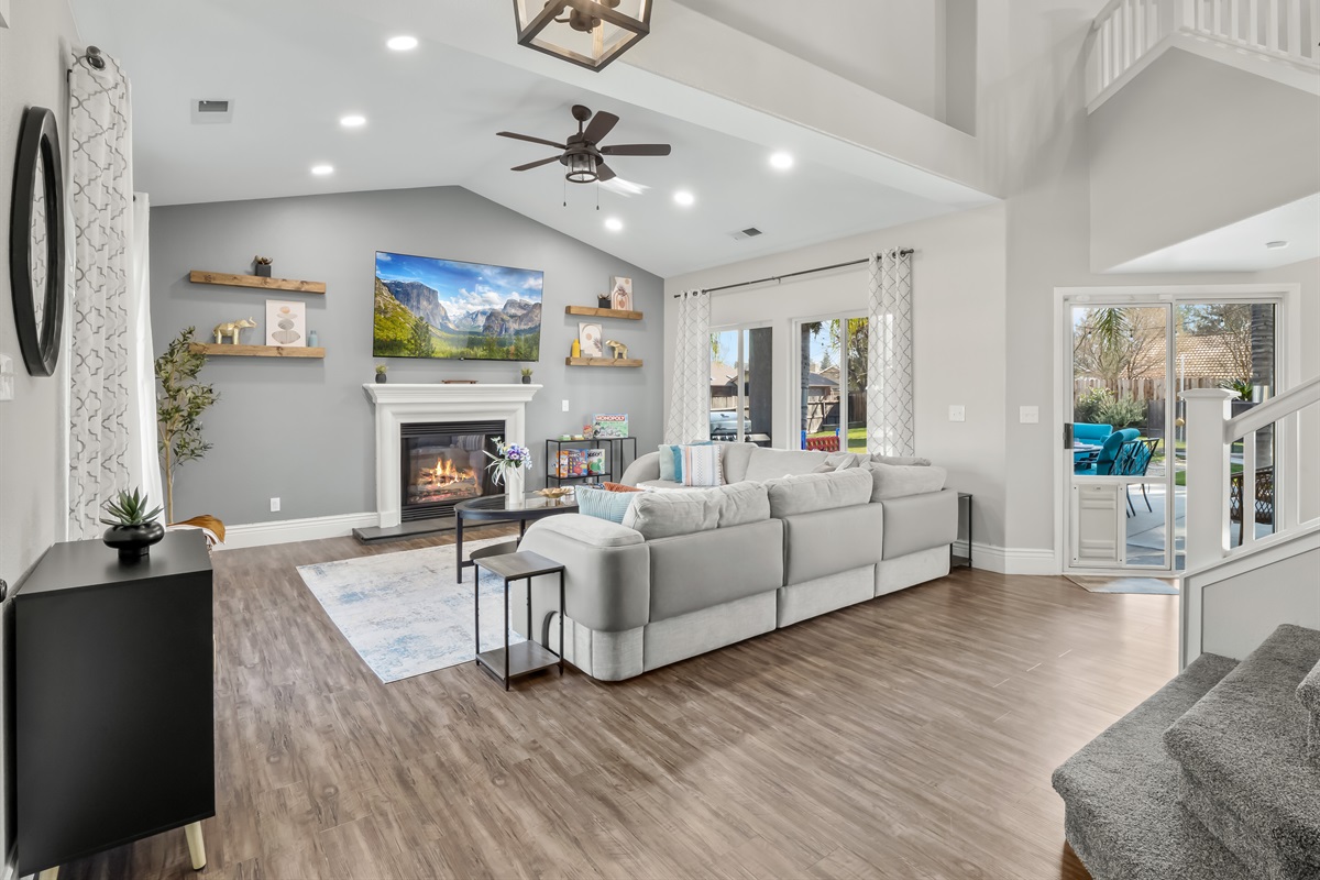 Spacious great room with vaulted ceilings, a cozy fireplace, and oversized sectional seating—perfect for family movie nights, board games, and gathering together after a fun day outdoors.