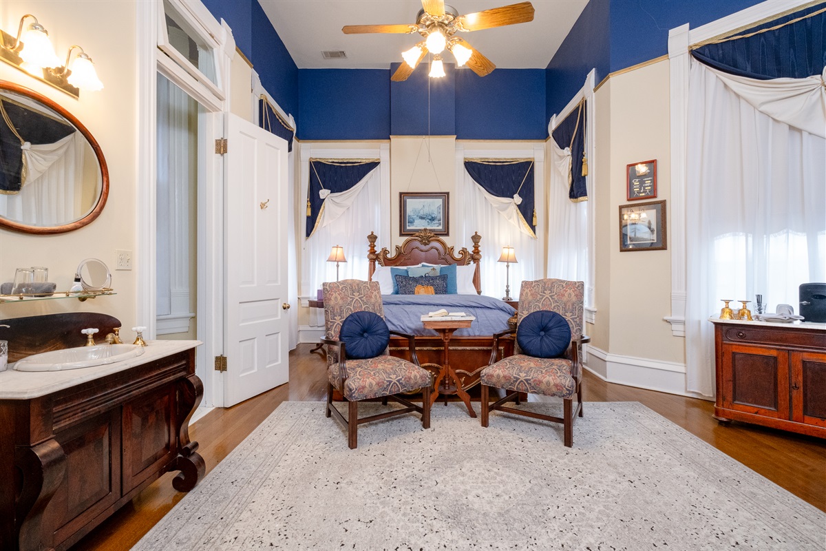 View toward the sleeping area, highlighting the room’s high ceilings, blue accent walls, and seating nook.