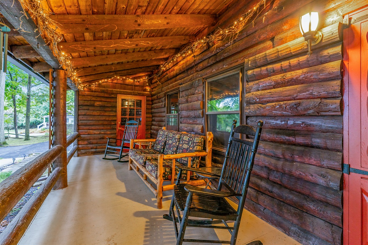 Relax on the covered porch with rocking chairs, rustic log seating, and warm ambiance perfect for morning coffee or evening sunsets.