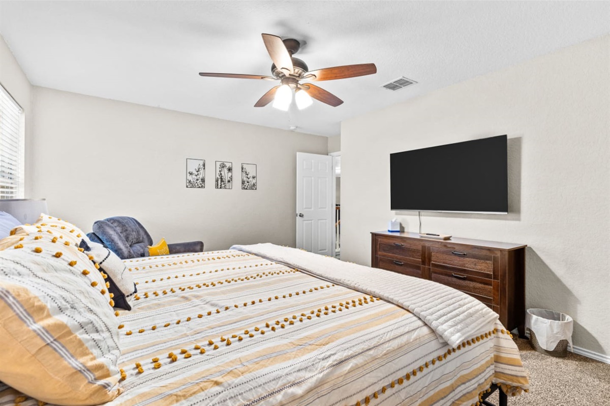 Secondary king bedroom designed for comfort with AC, ceiling fan, blackout blinds, extra pillows, Smart TV with streaming, and a cozy sofa chair for relaxing.