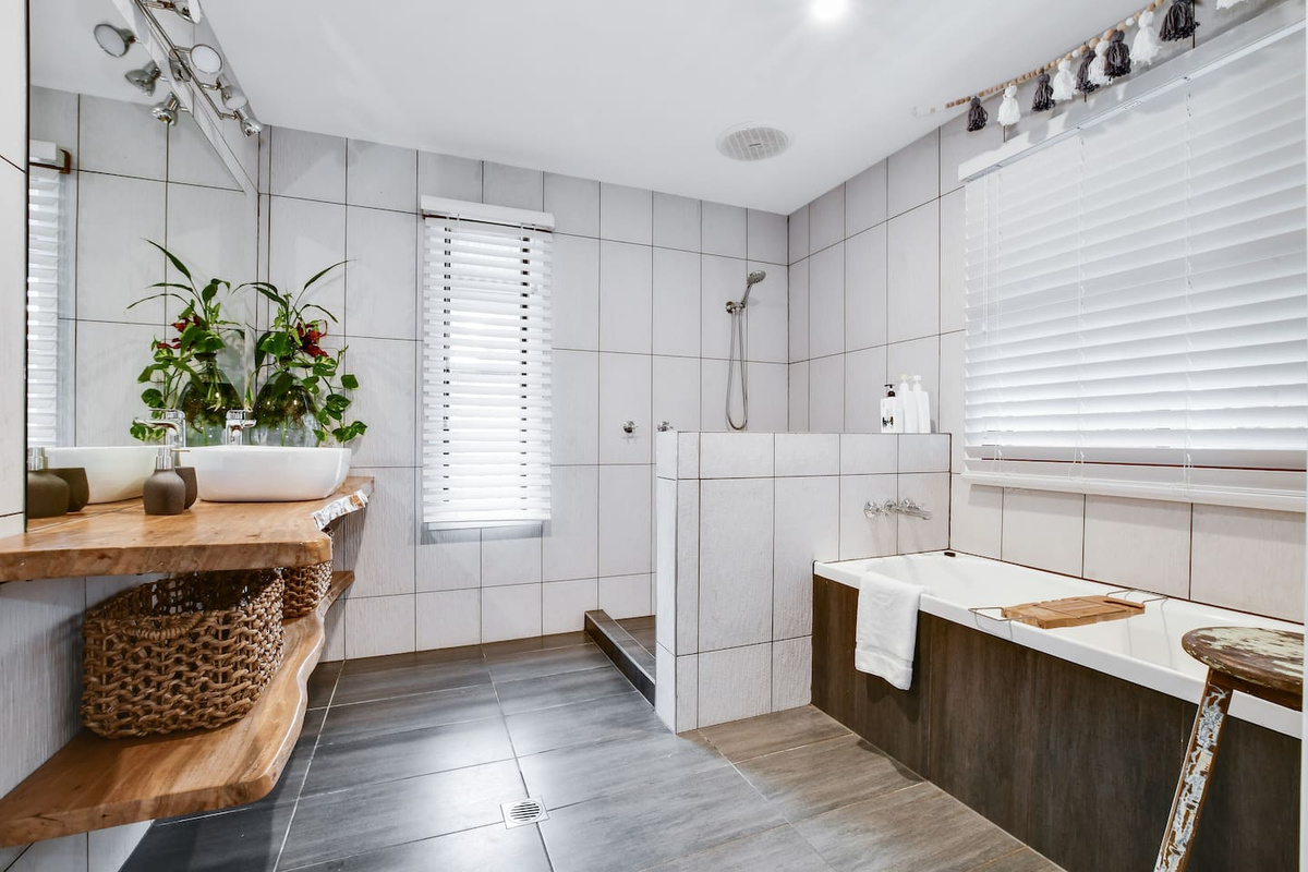The natural-edge timber vanity and freestanding-style bath surround give this bathroom at Aaron's Beachside Boat House plenty of distinctive beach-house character.