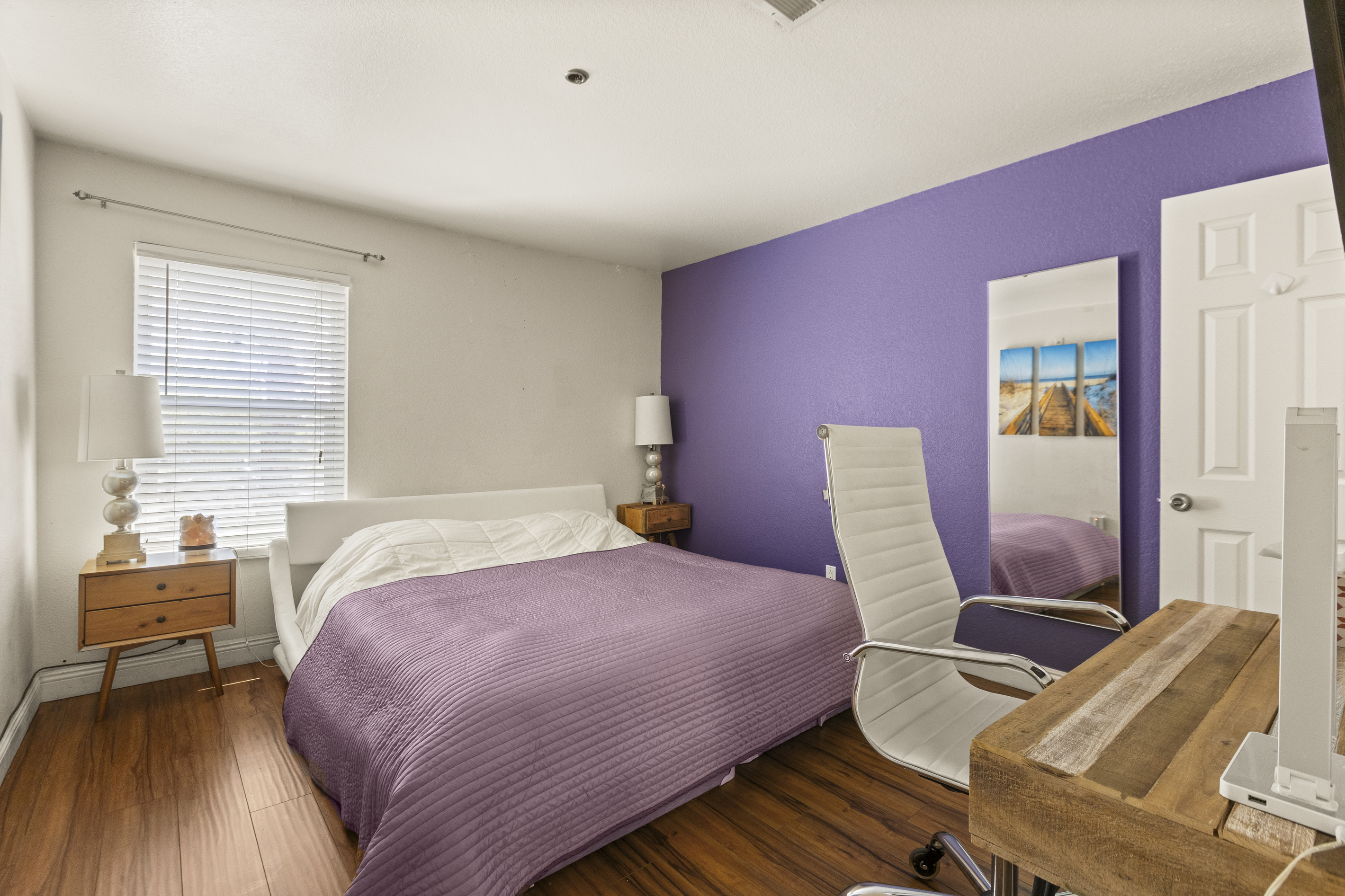 Bedroom  2 with with purple king bedding, matching accent wall, desk workspace, and a chair for working or getting ready.