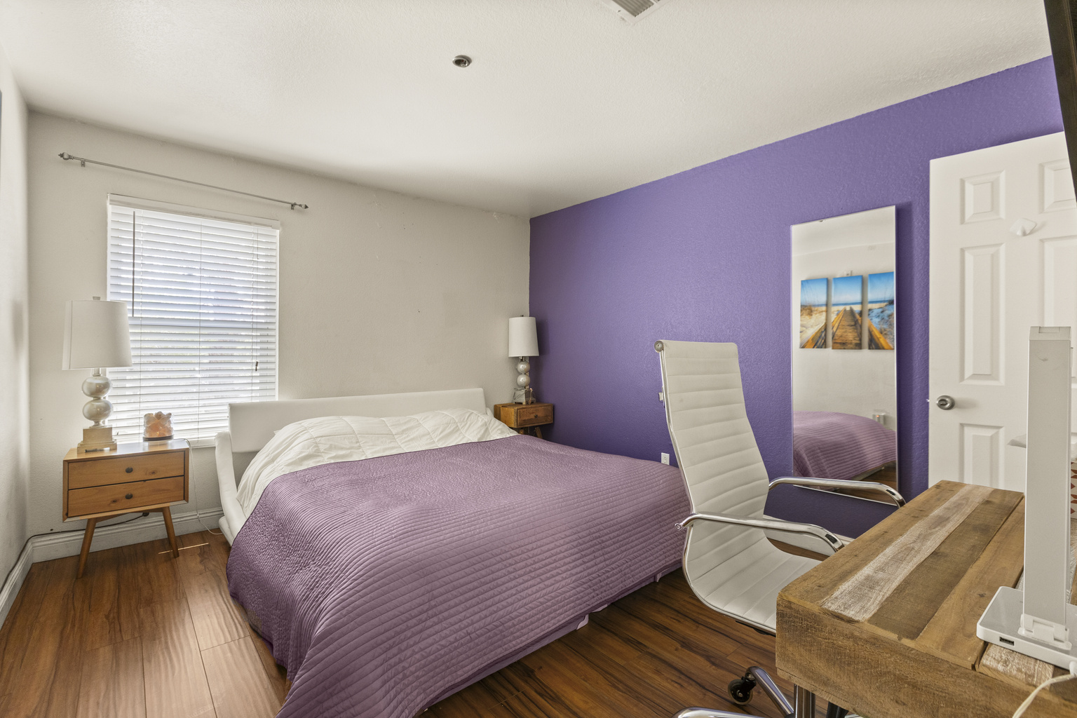 Bedroom  2 with with purple king bedding, matching accent wall, desk workspace, and a chair for working or getting ready.