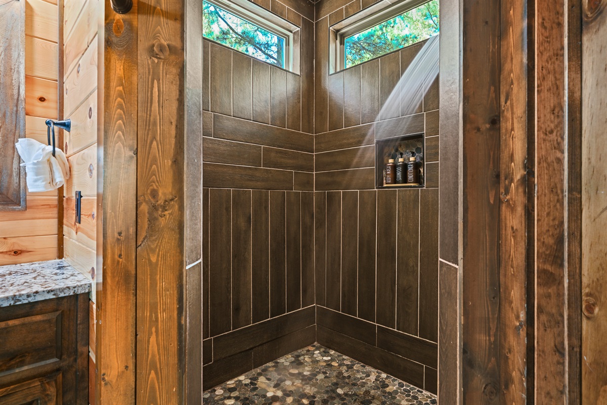 A walk-in shower with natural wood tones and rainfall showerhead offers a spa-like start or end to your day.