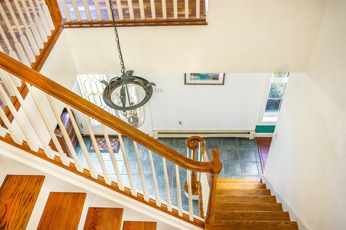 Step into a grand formal foyer that sets the tone for your Southwest Harbor stay. This colonial-style entryway features a turning oak staircase and a custom lighting fixture, offering a bright, welcoming arrival for your Acadia National Park getaway.