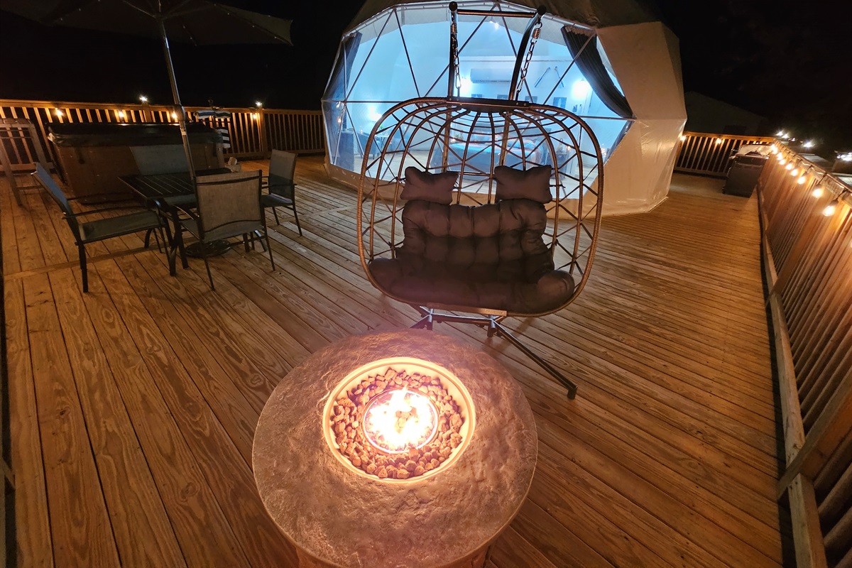 Cozy nighttime deck with fire pit, egg chair, hot tub, and the dome glowing softly for the perfect romantic escape
