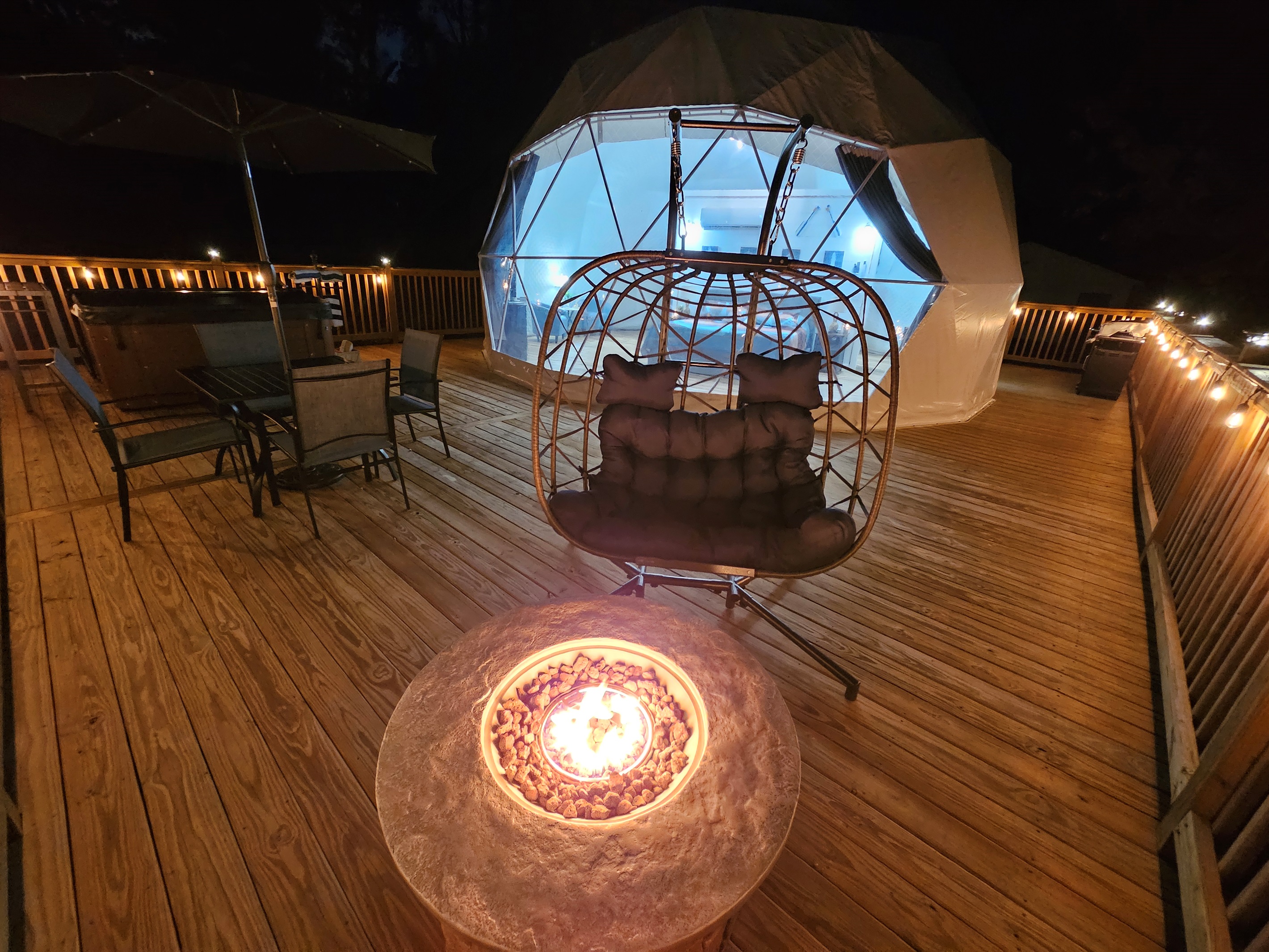 Cozy nighttime deck with fire pit, egg chair, hot tub, and the dome glowing softly for the perfect romantic escape