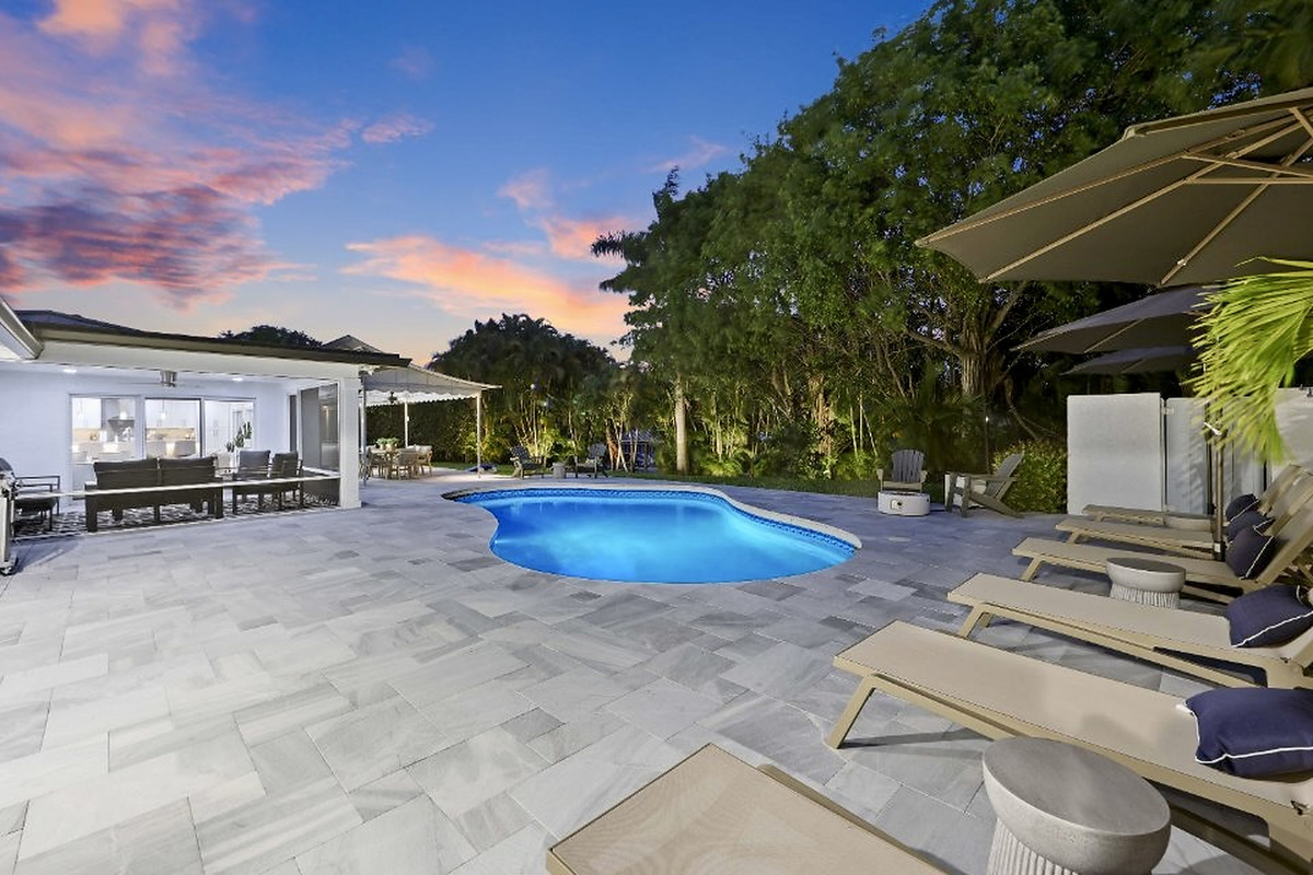 Enjoy shaded outdoor dining beside the pool, with lawn, palms, and canal-side greenery creating an easy indoor-outdoor vacation feel.