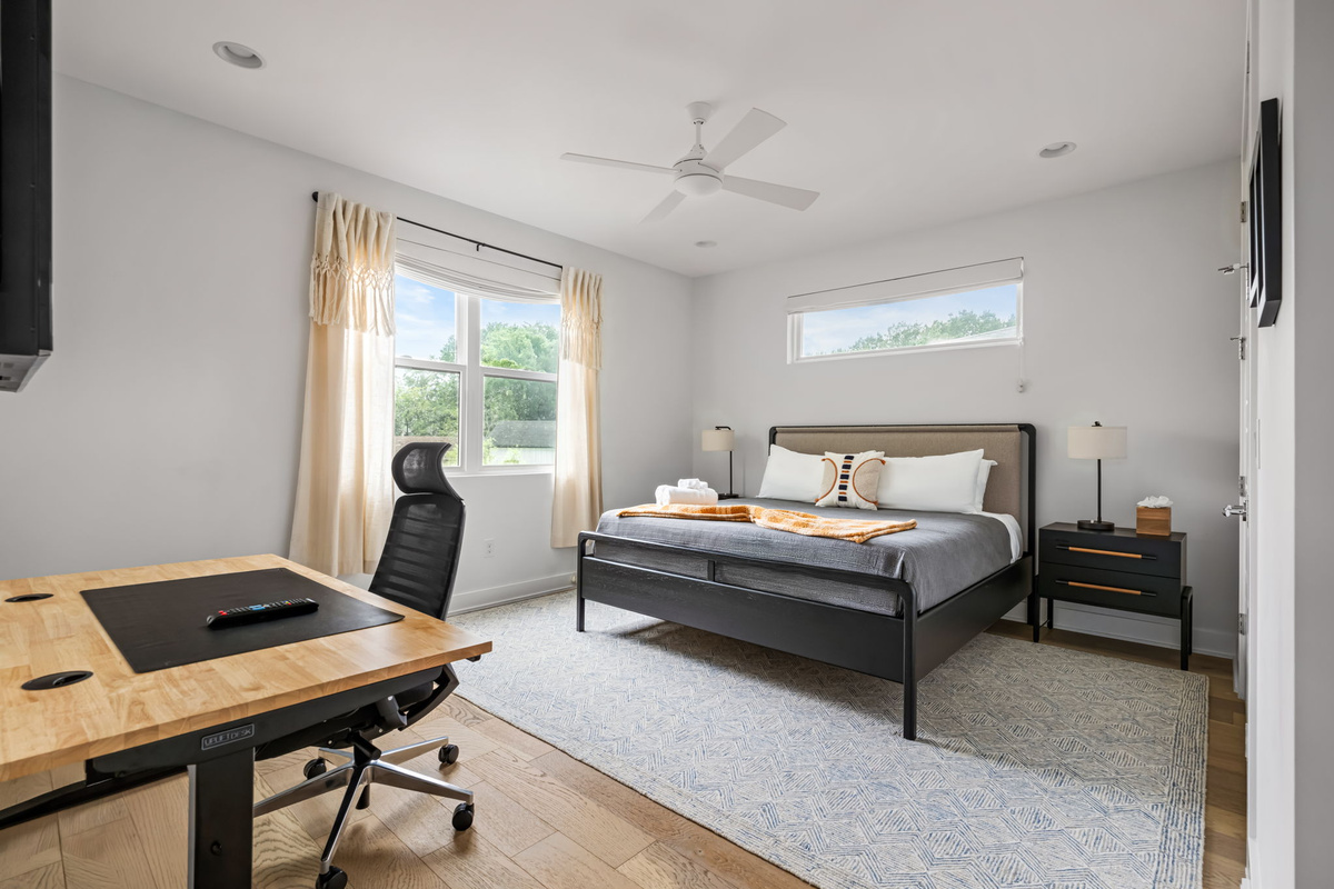 Sunlit bedroom featuring a cozy queen bed, dedicated work desk, and plush area rug — perfect for remote work or a peaceful night's sleep.