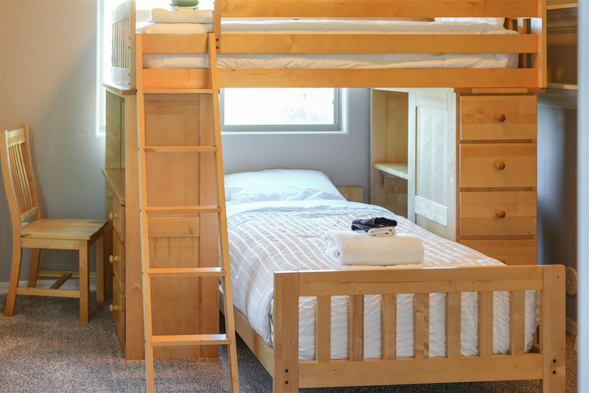 Comfortable lower bunk with fresh linens, ladder access to the top bunk, and nearby workspace.