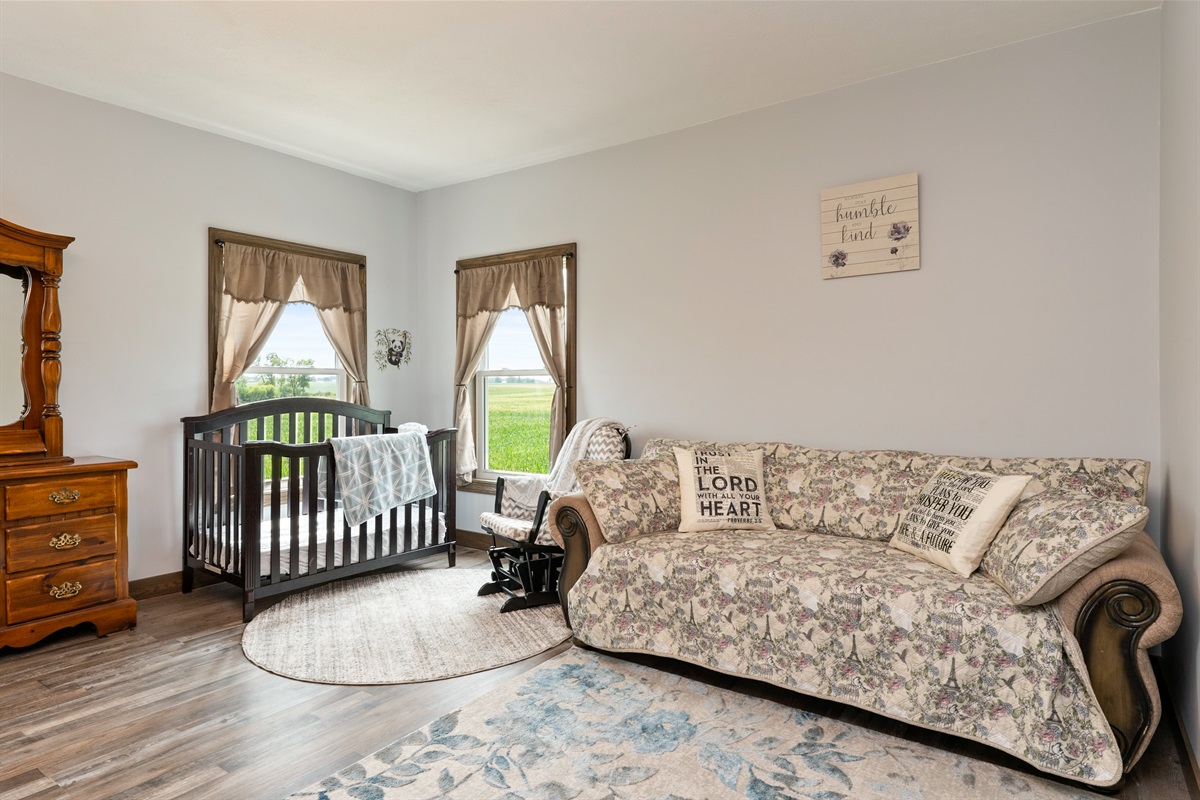 A bright and spacious master bedroom featuring a cozy queen bed, Queen fold out sofa and crib with elegant wood furniture, and stunning countryside views through large windows. Perfect blend of comfort and charm for a restful stay. Bedroom #1