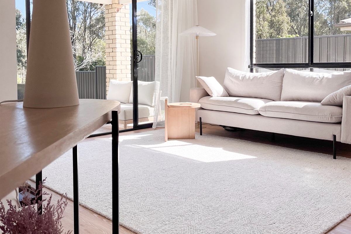 Summers Green View Retreat in Logan Reserve has a bright living room with soft seating, sheer curtains and views toward the backyard greenery.