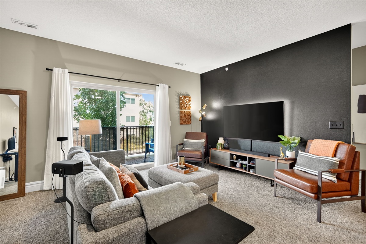 Stylish open-concept living with plush seating, leather accent chairs, and a smart TV. Natural light flows in from the balcony, blending modern comfort with chic design for the perfect stay.