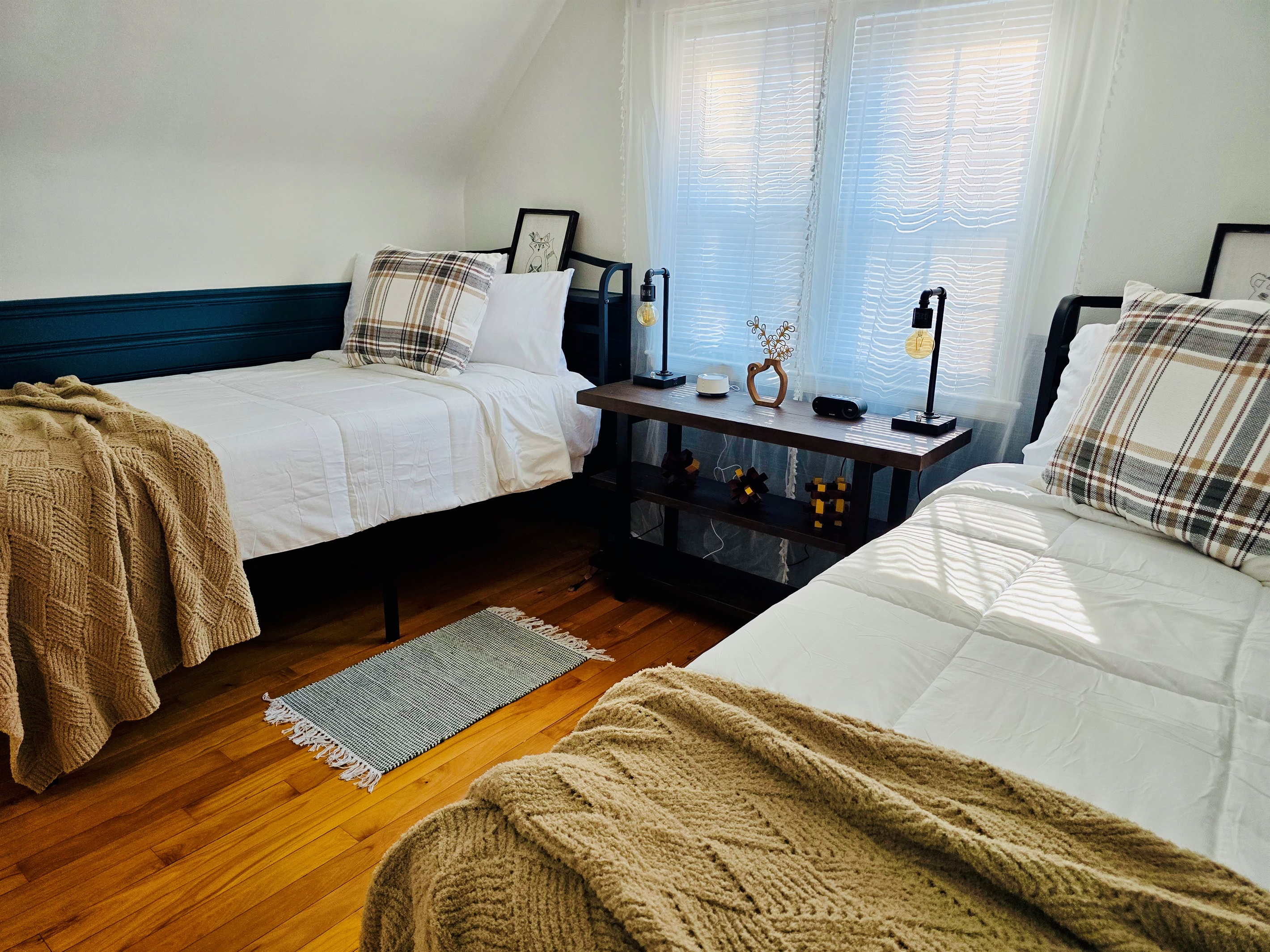 Twin XL beds with cozy lighting, charging stations, alarm clock, and white noise machine offer restful nights on rich hardwood floors. A wall-mounted TV (not pictured) adds entertainment, and an optional safety rail available for added peace of mind.