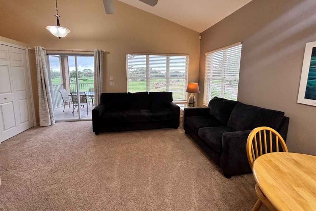 Spacious living area with comfortable seating, ceiling fan, large windows, and direct access to the private screened balcony.