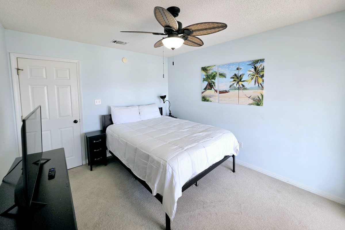 Bedroom with ceiling fan and beach-themed art
