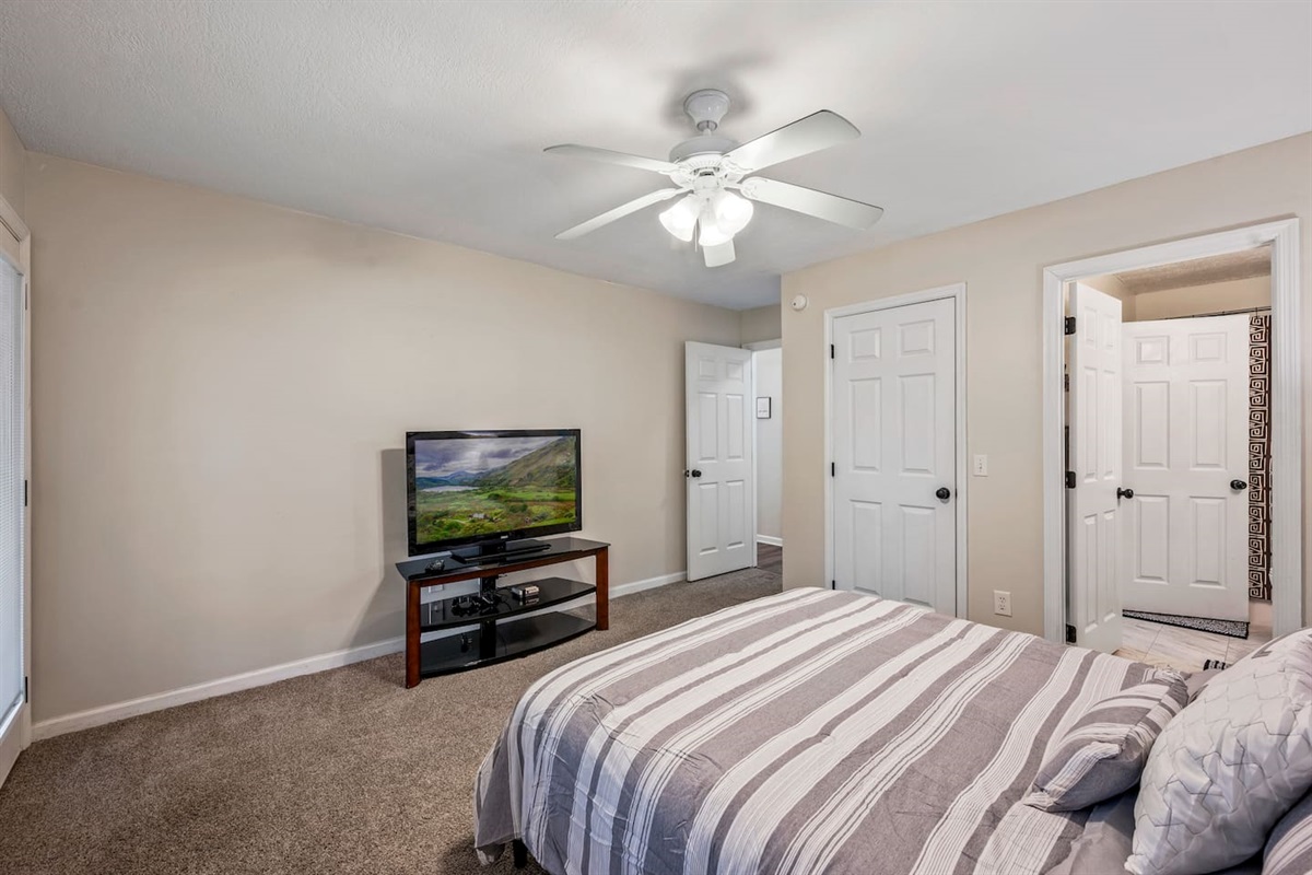 Cozy bedroom featuring a comfortable bed with fresh linens, ceiling fan, and a flat-screen TV for relaxing after a long day. The room includes easy access to a private bathroom and ample closet space for your convenience.
