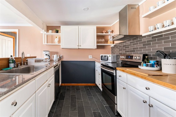 Kitchen features a dishwasher, microwave, coffee maker, tea kettle, stove/fridge, cooking utensils, and assorted pantry supplies like coffee, tea, sugar, olive oil, salt/pepper and others.