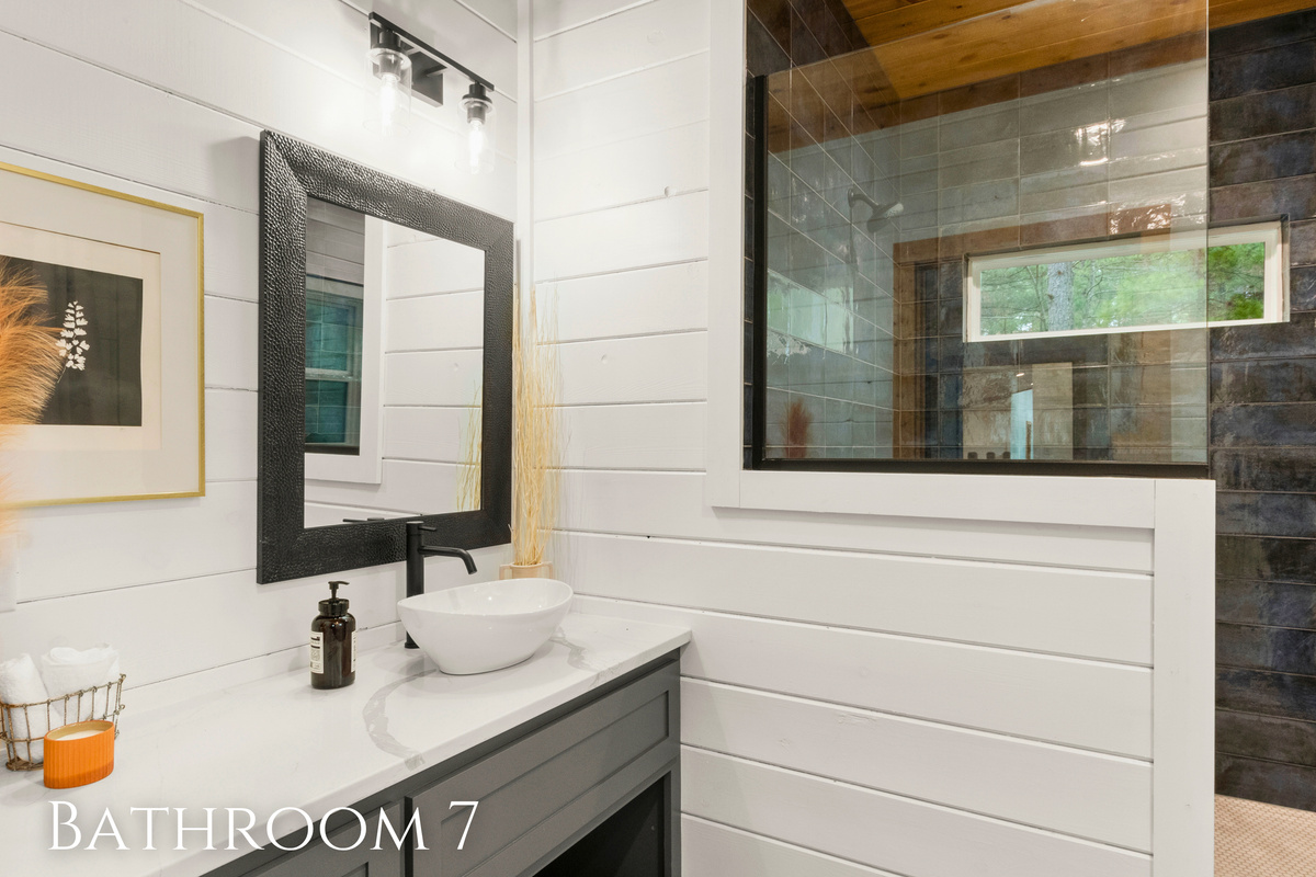 The bathroom exudes a clean and modern aesthetic, characterized by crisp white shiplap walls contrasted with a dark, textured tile in the shower.