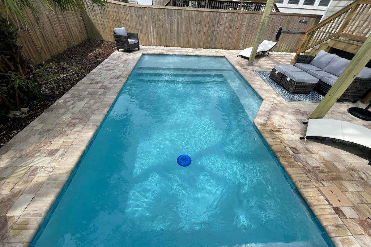 Seen from the porch stairs, the pool stretches long enough for real laps — with a shallow shelf for waders, loungers for sun-chasers, and a cushioned outdoor sectional for the umbrella-drink committee.