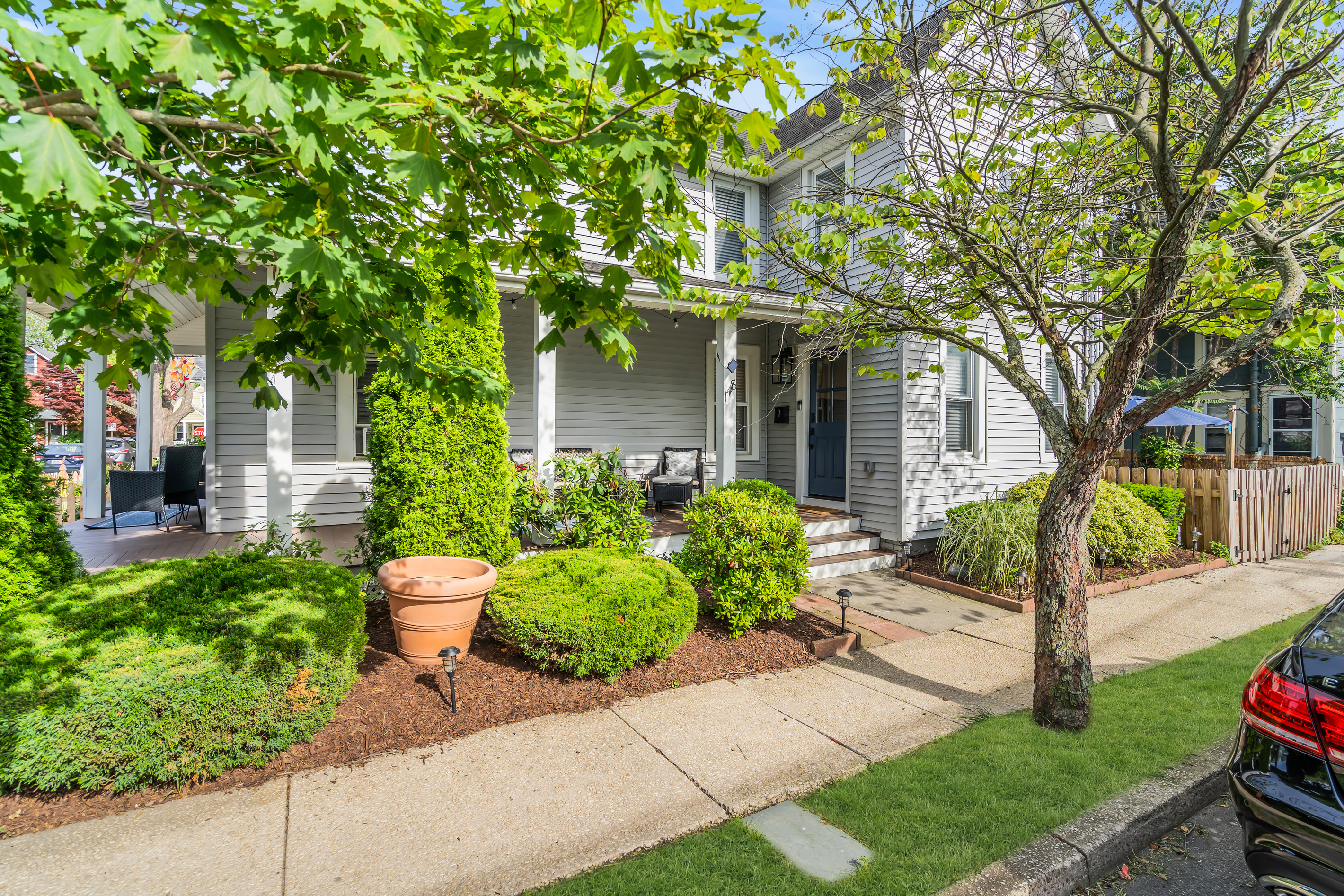 Picture pulling up to this every time you come back. The navy door, the wicker chair, and the flowering shrubs make the welcome feel warm before you even step in.