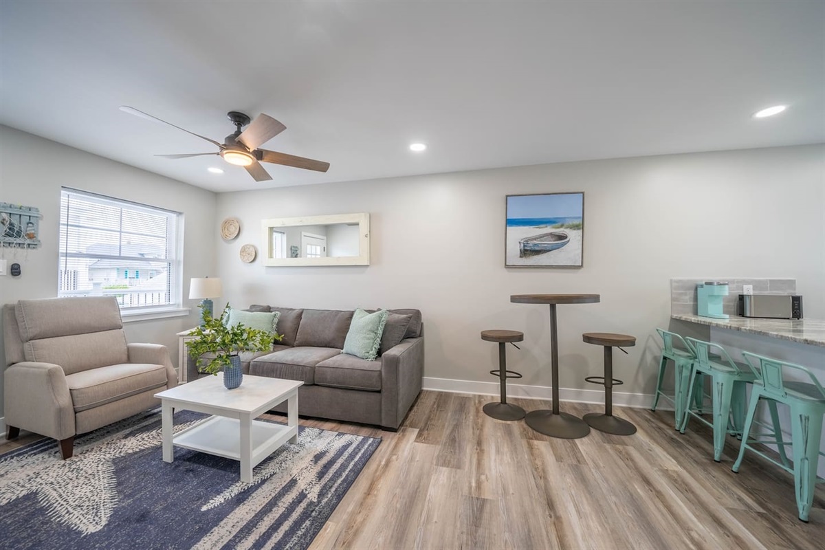 Open concept living and dining area with comfortable seating, ceiling fan, and soft natural light. The space connects easily to the kitchen and breakfast bar, offering a relaxed setting for lounging, casual meals, or planning the day.
