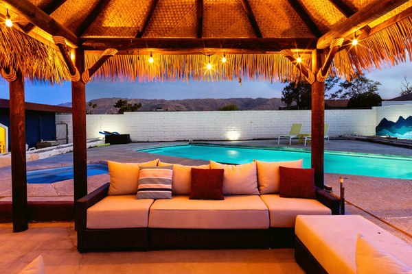 Private pool and palapa lounge at dusk under string lights, near Joshua Tree National Park. The in-ground spa is not in service