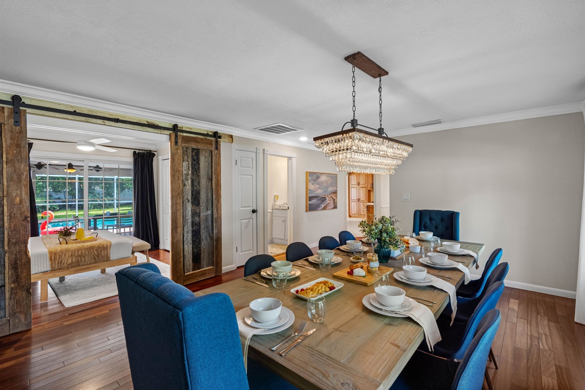 Elegant dining room featuring a rustic wood table, plush blue chairs, and a sparkling chandelier centerpiece.