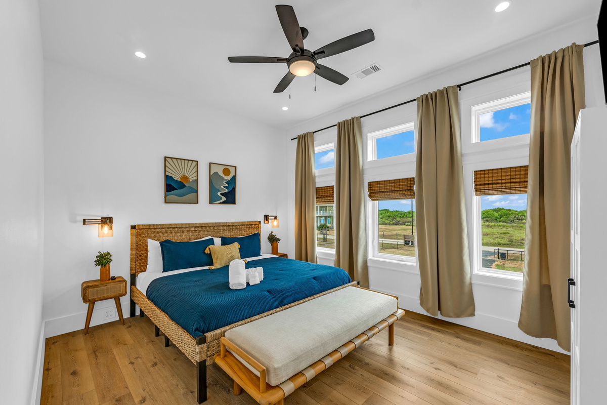 Cair Paravel: Navy blue bedding and sunrise-toned art play against warm wood floors and a wall of windows. 