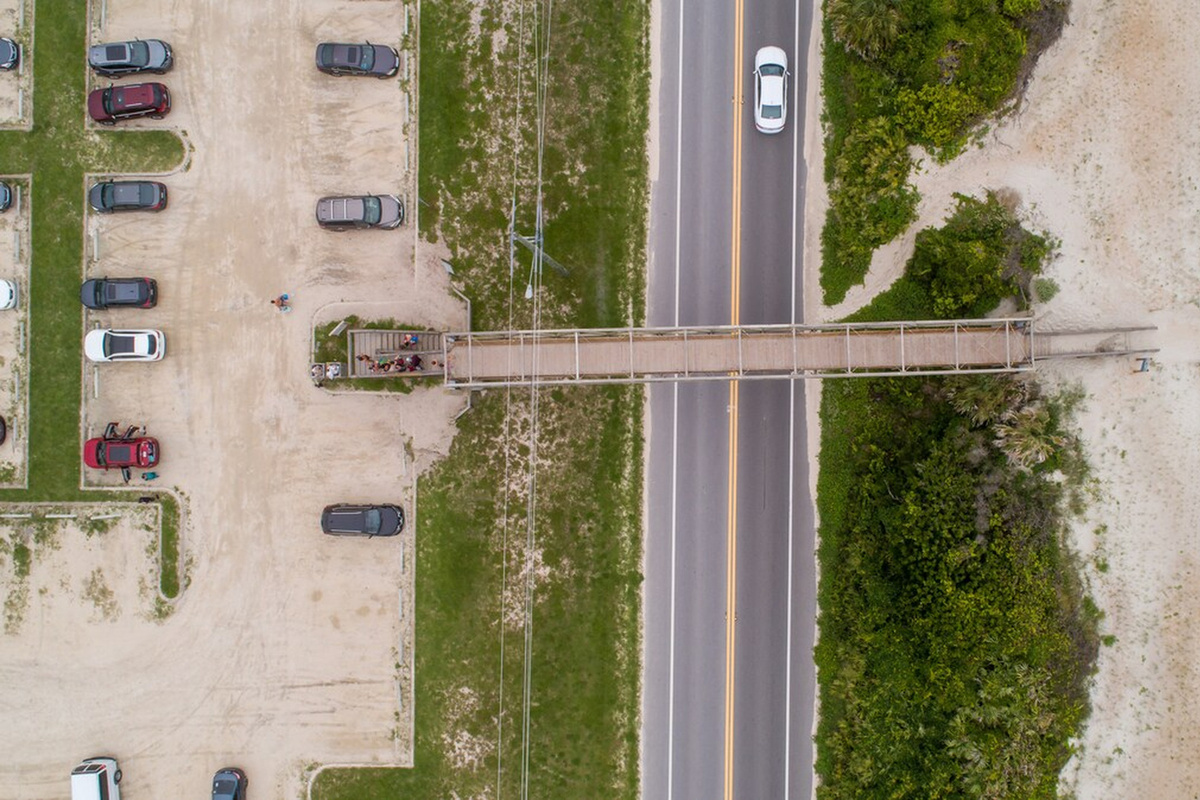 The walkway seen from above, with the car park on one side and dunes and open sand on the other. Roughly eight to ten minutes on foot from the front door, chairs and boogie boards rattling in the wagon behind you.
