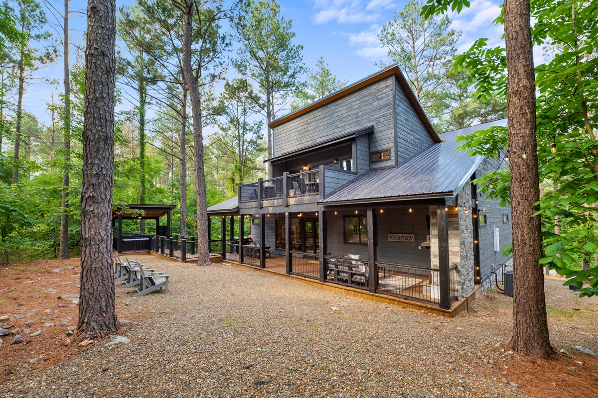 Rear exterior view of a multi-level cabin with a covered deck and outdoor seating in a woodland setting