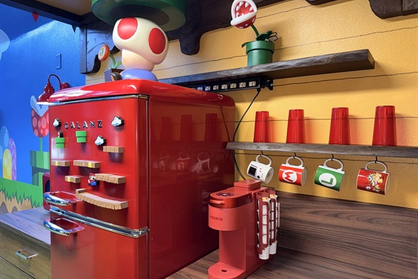 Retro red fridge and coffee station at Mario's Mini Mansion in Clermont, FL! Toad peeking over the top, colorful hanging mugs, and playful Super Mario accents bring joy to every morning brew and snack time.