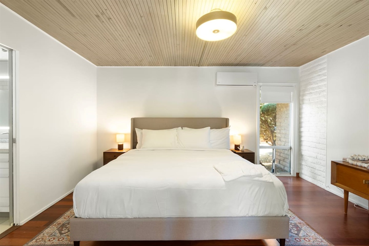 Serene primary bedroom with a comfortable king bed, warm wood ceilings, and soft ambient lighting for a relaxing retreat.