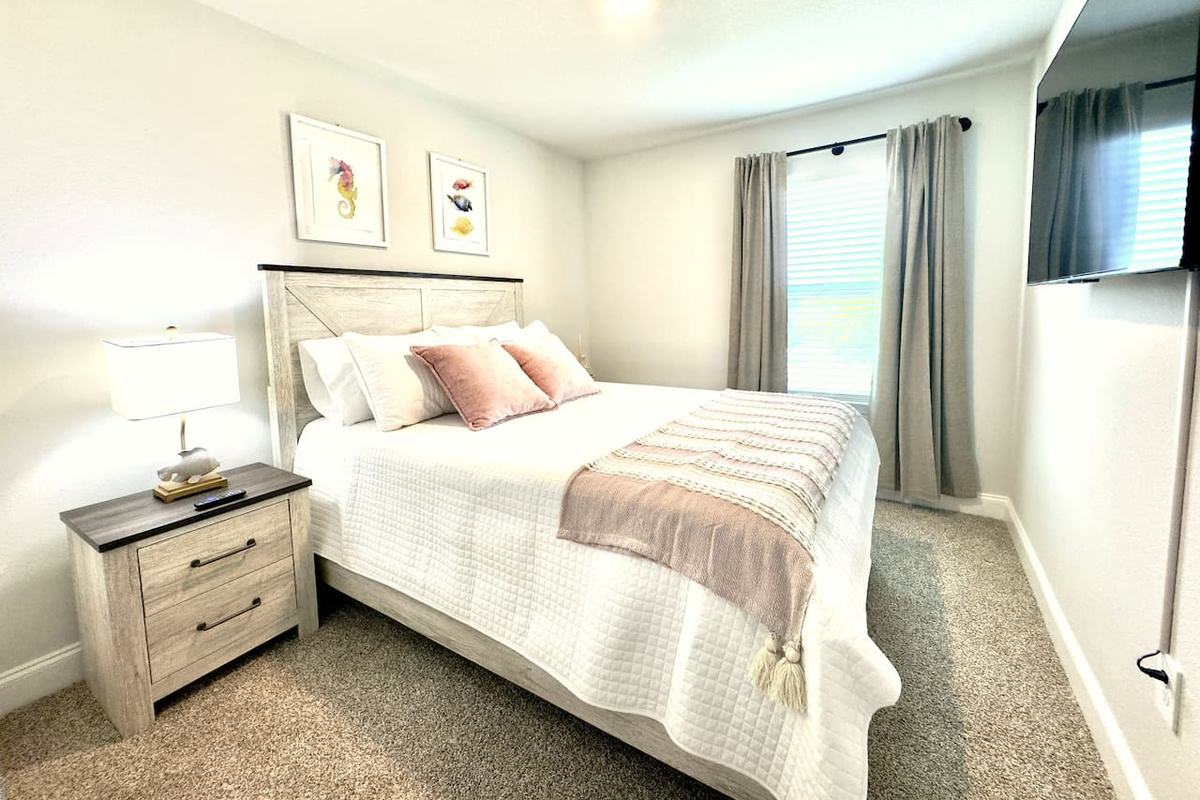 Exhausted, you sink into this bed — plush white linens, soft accent pillows cradling you, plush carpet beneath tired feet. Through the sheer curtains, soft daylight glows gently. Quiet, cocooned, ready to rest.