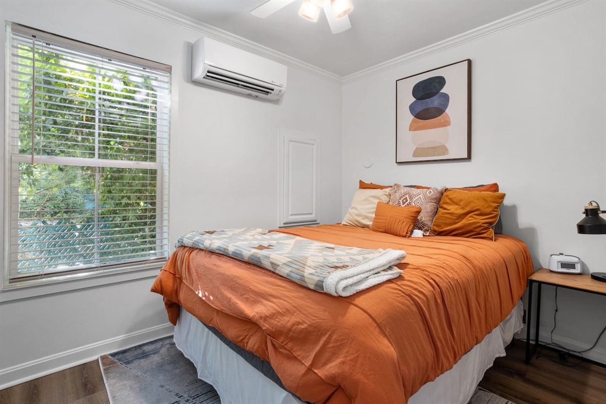 Queen size bed with night lamp, alarm clock/sound machine, and mini split A/C